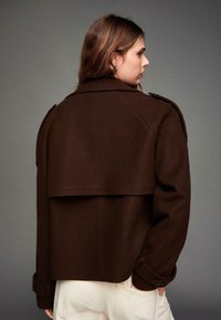 Veste en mélange de laine marron avec une silhouette structurée, un col oversize et des épaulettes. Présente un design à dos court et des manches à poignets.