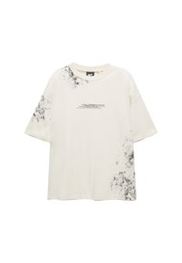 Tricou supradimensionat bej deschis cu design în stropi negri. Are guler rotund și mâneci scurte, fiind confecționat din bumbac moale și respirabil.