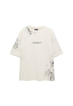 Lichtbeige oversized t-shirt met zwart spetterontwerp. Heeft een ronde hals en korte mouwen, gemaakt van zachte, ademende katoen.