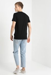 Camiseta de algodón negra con cuello redondo clásico, combinada con jeans de mezclilla azul claro y zapatillas grises. Diseño simple y casual.