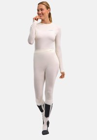 Haut thermique blanc à manches longues et bas taille haute en tissu texturé. Présente des chaussettes sombres contrastantes et des accents de marque subtils.