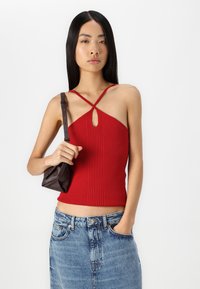 Top de tirantes rojo acanalado con un diseño de ojal y tirantes cruzados, combinado con una falda de mezclilla y un pequeño bolso de cuero marrón.