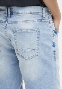 Jeans de mezclilla azul claro con un ajuste relajado, que cuentan con dos bolsillos traseros, un desvanecimiento sutil y un patrón triangular cosido en los bordes de los bolsillos.