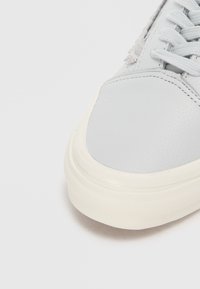 Sneaker gri din piele cu o parte superioară texturată, șireturi gri deschis și o talpă din cauciuc alb. Prezintă cusături subtile și un finisaj neted.