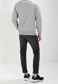 Szara bluza z prążkowanymi mankietami i ściągaczem u dołu, zestawiona z czarnymi dżinsami z lekkimi przetarciami i podwiniętymi nogawkami. Całość dopełniają czarne buty sportowe.