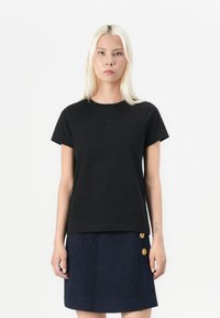 Black cotton t-shirt with a round neckline and short sleeves, featuring a subtle logo detail on the chest. Paired with a textured navy skirt.