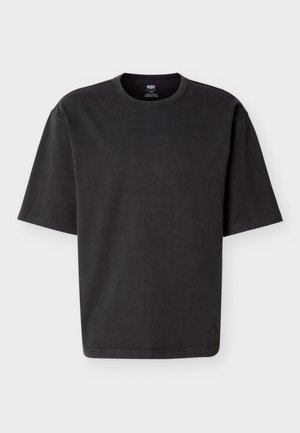 Χαλαρό, μαύρο κοντομάνικο T-shirt Levi's με στρογγυλή λαιμόκοψη και εμφανές ετικέτα γιακά σε απλό φωτεινό φόντο.