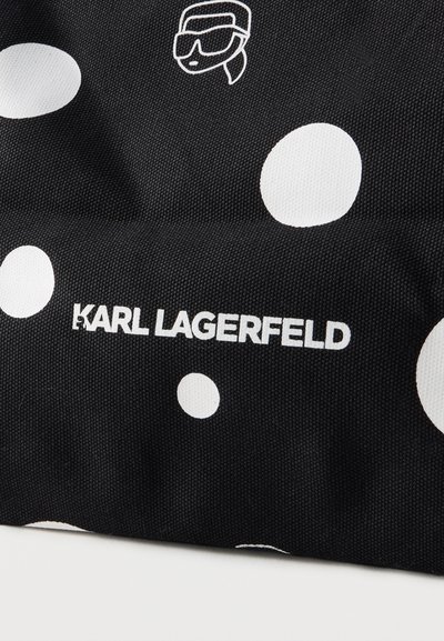 Черен плат с големи бели точки на точки, бял текст "KARL LAGERFELD" и малка бяла графика на човек със слънчеви очила и опашка.