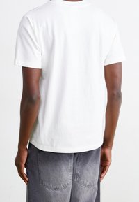 Person wearing a plain white short-sleeve T-shirt and faded gray denim pants, shown from the back against a white background.