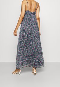 Maxi-jurk met een bloemenprint in blauw, groen, roze, met een gerimpelde achterkant en dunne schouderbandjes, gecombineerd met witte blokhak sandalen.