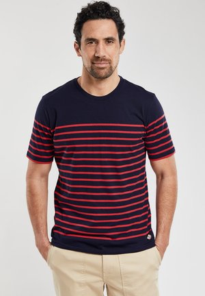 Mørkeblå t-shirt med røde vandrette striber, rund halsudskæring, korte ærmer, og et mærke på venstre side forneden. 100% bomulds materiale.