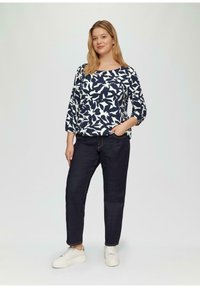 Marineblauw top met wit bloemenpatroon, 3/4 mouwen; gecombineerd met donkere jeans en witte sneakers met een textuurrand. Casual outfit.