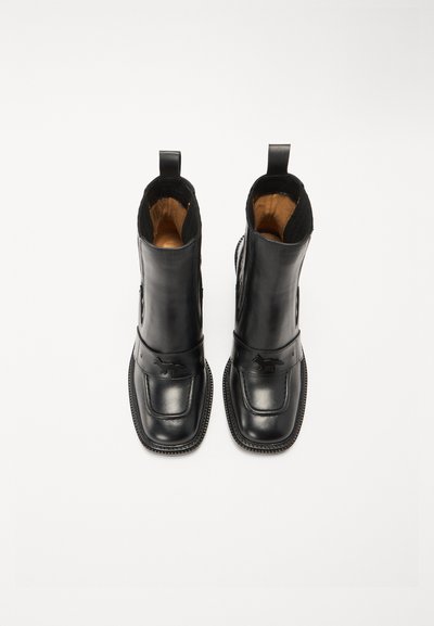 Botas de ante negro con un acabado suave, paneles laterales elásticos y costura decorativa a lo largo de la suela. El interior es de color marrón claro.