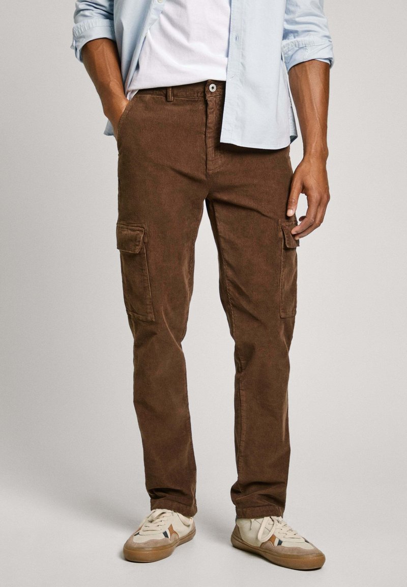 Pantalones cargo marrones hechos de suave algodón, con dos bolsillos laterales, corte regular y una textura sutil. Combinados con zapatillas ligeras.