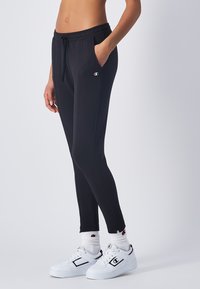 Pantalones joggers deportivos negros con una cinturilla elástica, bolsillos laterales y un diseño ajustado. Combinados con zapatillas blancas y calcetas con canalé.