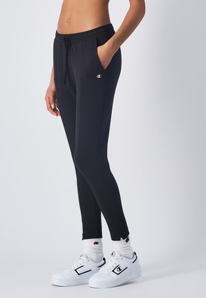 Pantalones joggers deportivos negros con una cinturilla elástica, bolsillos laterales y un diseño ajustado. Combinados con zapatillas blancas y calcetas con canalé.