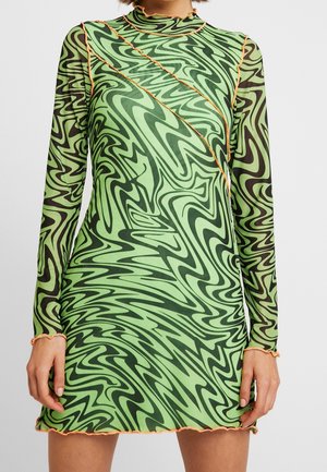 Mini-robe à manches longues avec motif ondulé vert et noir, bordure orange le long des coutures, de l'encolure, des poignets et de l'ourlet.