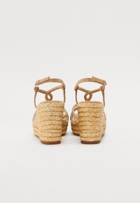 Hæl sandaler med en vevet stråsåle, brune ankelstropper, og en krystallakkent på sidene, designet for heving og støtte.