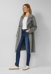Szary płaszcz z mieszanki wełny z dużymi klapami i dwurzędowymi guzikami, w połączeniu z ciemnoniebieskimi obcisłymi dżinsami i białymi trampkami.