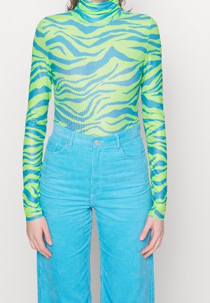 Col roulé à manches longues imprimé zèbre vert citron et bleu, associé à un pantalon en velours côtelé bleu clair taille haute.