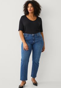 Top nero a maniche corte con scollo a V abbinato a jeans in denim blu a vita alta. I jeans sono dritti, con una texture e presentano un classico design a cinque tasche.