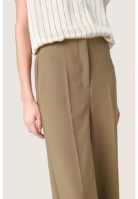 Pantaloni beige a vita alta, a gamba larga, in un tessuto liscio, con tasche laterali e una cucitura frontale pulita, abbinati a una maglietta a righe.