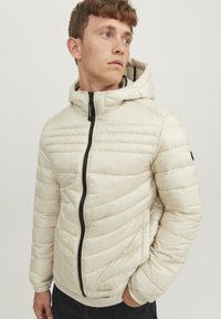 Padded jacket in light cream, featuring a hood, black front zipper, and ribbed cuffs. The design includes horizontal stitching patterns.
