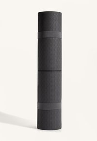 Svart yogamatta med texturerad yta i fiskbensmönster. Rullad och säkrad med ett grått elastiskt band. Kompakt cylindrisk form.