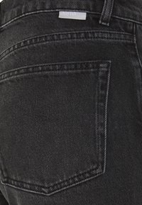 Poche arrière d’un jean en denim noir avec des coutures doubles et une petite étiquette en tissu blanc au-dessus de la poche.