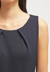 Abito senza maniche di un blu scuro con un collo rotondo, caratterizzato da dettagli plissè e una texture liscia, che mette in risalto una vestibilità sartoriale.