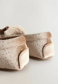Chaussons en velours marron avec un intérieur doux, ornés de points argentés. Forme arrondie, petit talon discret et semelles texturées pour une meilleure adhérence.