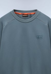 Hemdblauwe sweatshirt met ronde hals, textuurstof en een klein, reliëf logo dat op een vlag lijkt op de borst. Oranje accenten aan de binnenkant van de kraag.