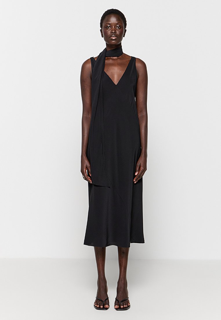 Czarna sukienka bez rękawów z dekoltem w kształcie litery V, zwiewna sylwetka i upięcie materiału przy szyi. Gładki, lekki materiał, długość do połowy łydki.