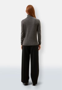 Grauer Rollkragenpullover mit weicher Textur, kombiniert mit schwarzen, weit geschnittenen Hosen. Das Design hat eine taillierte Silhouette und lange Ärmel.