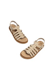 Beige Wildledersandalen mit mehreren gekreuzten Riemen, offenem Rücken und flacher Sohle, die gestickte Details und einen kleinen verstellbaren Schnallenverschluss aufweist.