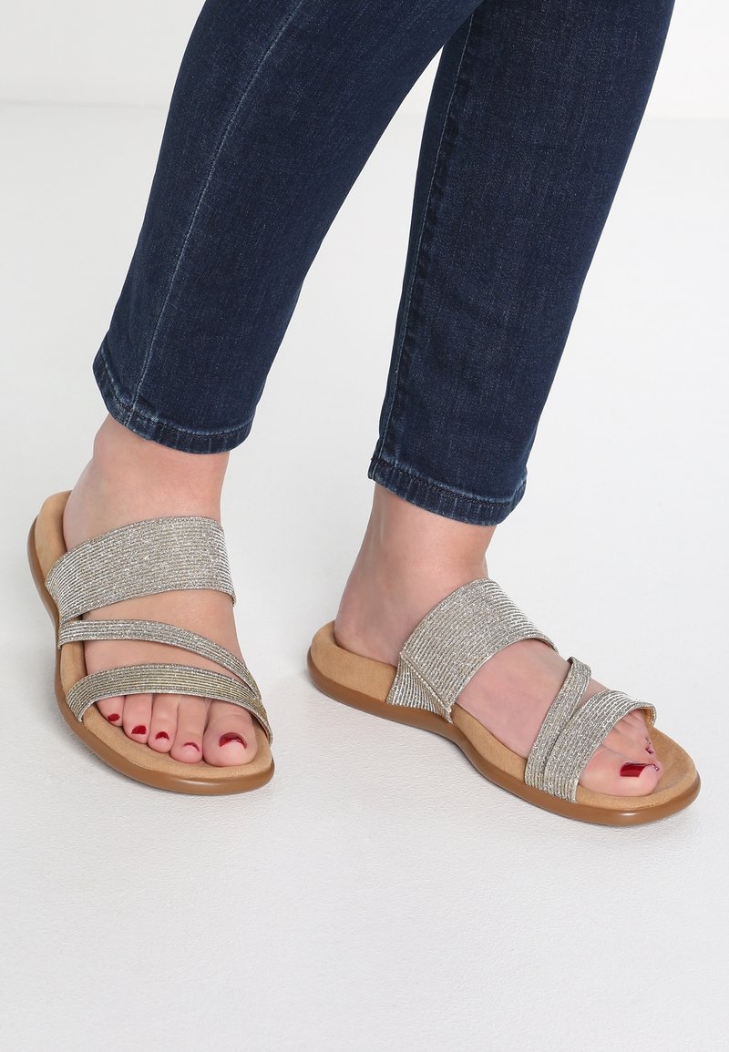 Sandales à glissière avec des brides argentées métalliques à finition texturée, posées sur une semelle beige ; design à bout ouvert mettant en valeur des ongles de pieds rouges polis.