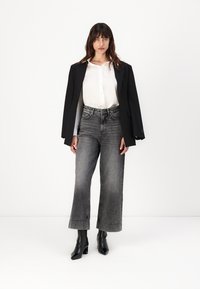 Blazer negro sobre una blusa blanca, combinado con jeans grises de tiro alto y pierna ancha, y botas negras de tacón abierto. Un look sencillo y estructurado.