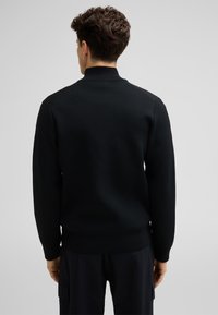 Zwarte gebreide trui met een hoge kraag, textuurpatroon, ribgebreide manchetten en onderrand. Heeft een slim fit en een minimalistisch ontwerp.