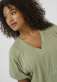 Blusa verde a maniche corte con scollatura a V, caratterizzata da dettagli plissettati sulle spalle e un tessuto morbido e testurizzato.