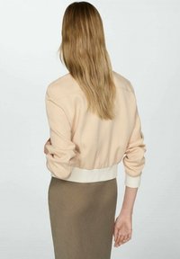 Světle růžová bomber bunda s žebrovaným bílým pasem a manžetami, s uvolněným střihem a měkkou texturou látky. Nositá s hnědou sukní.