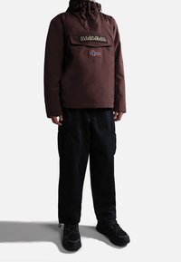 Braune Kapuzenjacke mit einer Fronttasche und einem norwegischen Flaggenpatch. Kombiniert mit schwarzen Cargo-Hosen und robusten schwarzen Schuhen.