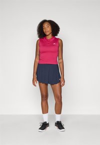 Polo senza maniche rosa con colletto, abbinato a una gonna a pieghe blu navy. Scarpe da ginnastica nere e calze bianche completano l'outfit.