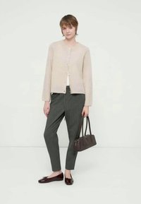 Cardigã bege claro em malha com decote redondo e fecho de botões, combinado com calças cinza às riscas e sapatilhas castanhas. Mala castanha incluída.