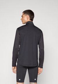 Langermet svart treningsgenser med høy krage. Laget av glatt, elastisk materiale. Båret med sorte shorts med to hvite prikker.