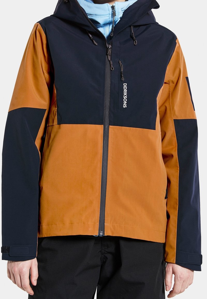 Color-blocked jacket featuring navy blue and brown sections, made from a durable material with a zippered front, adjustable hood, and cuffs.