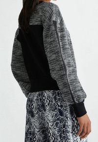 Felpa a maniche lunghe in bianco e nero con motivo, maniche testurizzate, orlo aderente e polsini a costine. Abbinata a una gonna a fantasia, che mostra un look a strati.