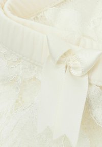 Spets tyg i off-white med ett satinbånd i form av en rosett. Har en mjuk, strukturerad yta och ett samlat elastiskt band.