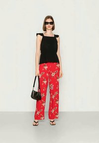 Top peplum preto com alças franzidas, combinado com calças soltas de padrão floral vermelho. Os acessórios incluem óculos de sol pretos e uma bolsa pequena.
