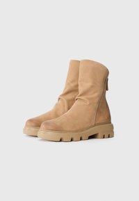 Bottines beiges en cuir souple et texturé, avec une semelle épaisse et une fermeture éclair à l'arrière. Design lisse pour l'avant et le dessus.