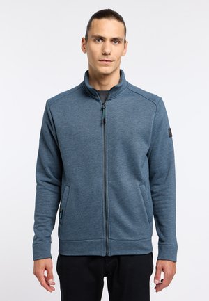 Blaues, mit Reißverschluss versehenes Jacket aus strukturiertem Stoff mit hohem Kragen, ausgestattet mit Seitentaschen und einem Logo-Patch am linken Ärmel.